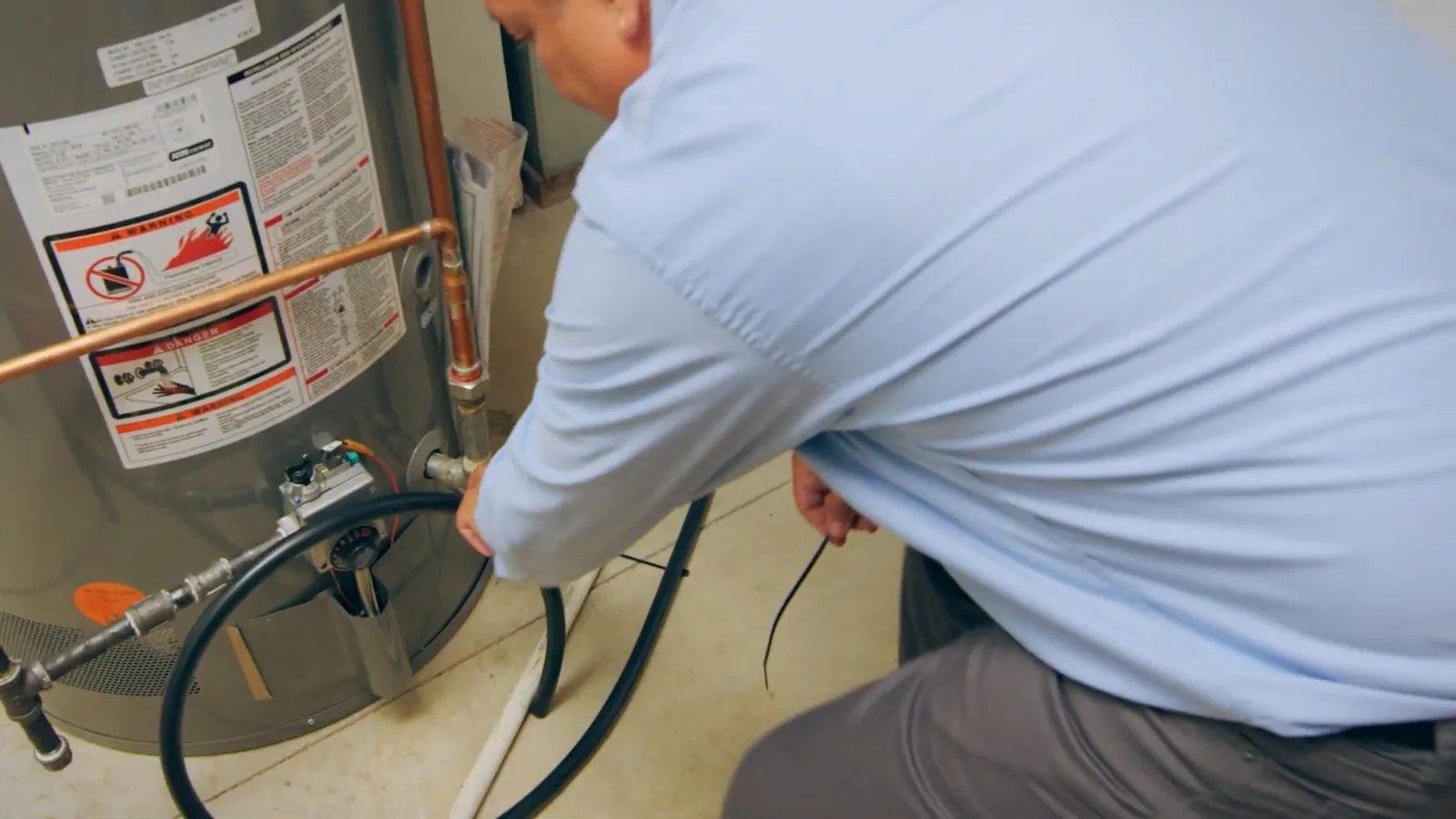 Technician in a light blue shirt crouching at a gas water heater to work on its connections